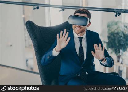 Young businessman wears VR headset glasses. Office worker or CEO sitting in company finance center lobby, testing new innovative method of managing business projects through virtual reality. Office worker sitting in company finance center lobby with VR headset glasses