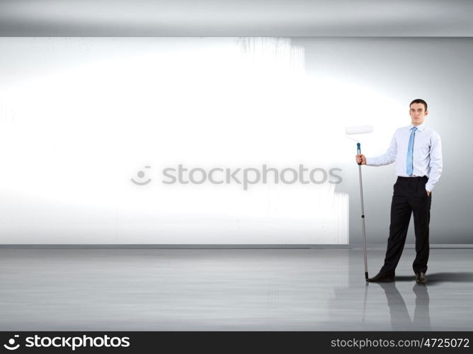 Young businessman with a paint brush against blank white wall