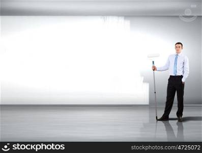 Young businessman with a paint brush against blank white wall
