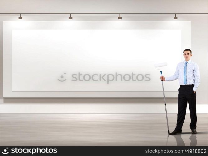 Young businessman with a paint brush against blank white wall