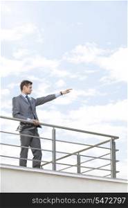 Young businessman with arm raised standing at terrace railings against sky