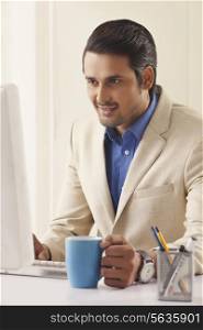 Young businessman with coffee cup working on computer at office desk
