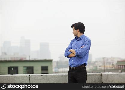 Young businessman with folded arms on city rooftop