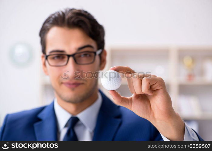 Young businessman with golf ball working in office