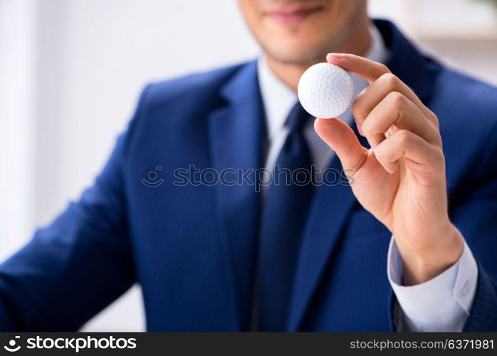 Young businessman with golf ball working in office