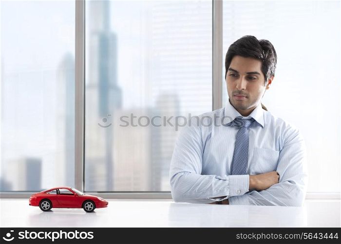 Young businessman with hands folded looking at car model