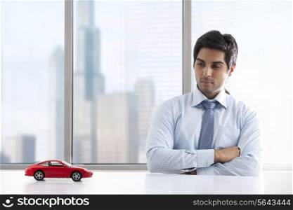 Young businessman with hands folded looking at car model