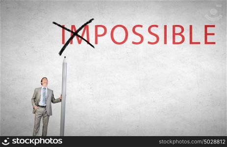 Young businessman with huge pencil changing word impossible. Nothing is impossible
