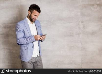 Young businessman with smartphone by the wall
