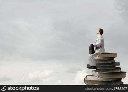 Young businessman with suitcase sitting on pile of old books. Knowledge advantage
