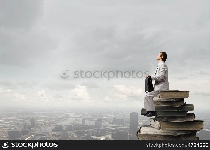 Young businessman with suitcase sitting on pile of old books. Knowledge advantage