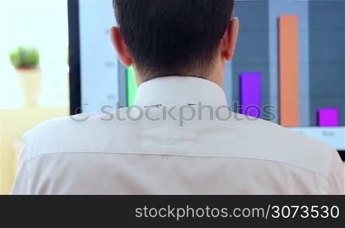 Young businessman working at the computer in the office. View from the back - dolly shot.