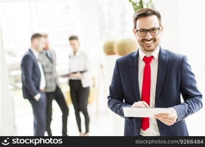 Young businessman working on a tablet while other young business people talking in the background