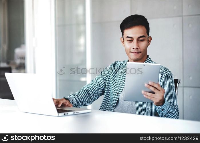 Young Businessman Working on Computer Laptop in Office. Smiling and looking at Digital Tablet