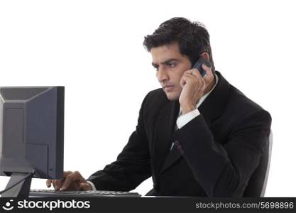 Young businessman working on computer while using cell phone