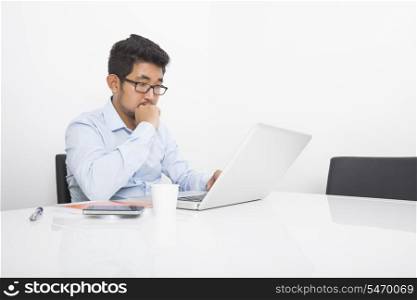 Young businessman working on laptop at desk in office