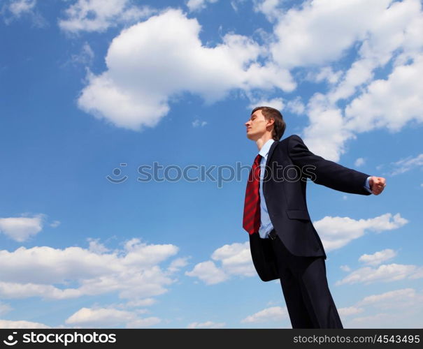 young businessmanin a blue suit embracing air against blue sky