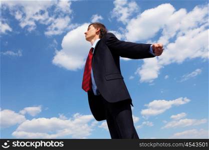 young businessmanin a blue suit embracing air against blue sky