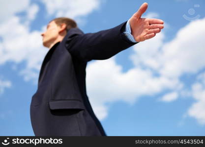 young businessmanin a blue suit embracing air against blue sky