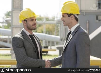 Young businessmen in hard hats shaking hands at construction site