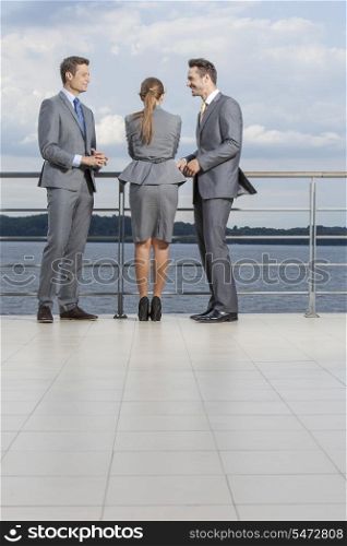 Young businesspeople standing at terrace railings against sky