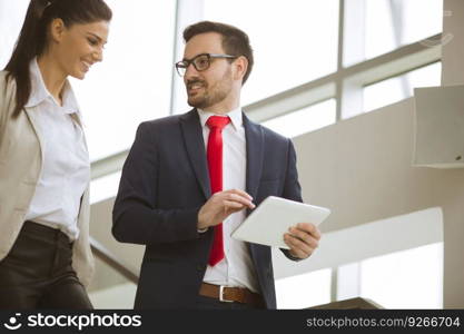 Young businesswoman and businessman walk down the stairs in office with a digital tablet in his hand