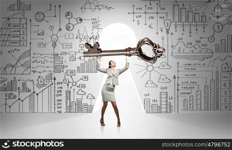 Young businesswoman and keyhole at background lifting big key above head. Find key to success