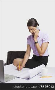 Young businesswoman answering mobile phone while working at desk over white background