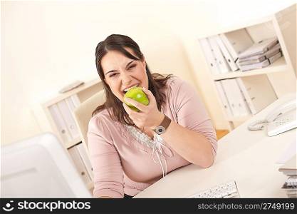 Young businesswoman biting apple at modern office