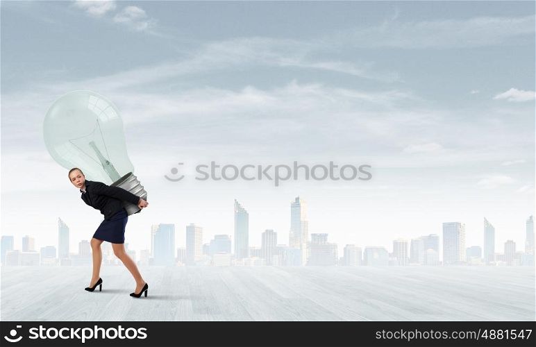 Young businesswoman carrying big light bulb on back. Carrying idea