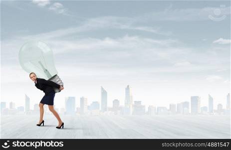 Young businesswoman carrying big light bulb on back. Carrying idea