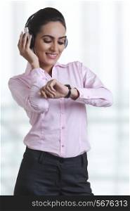 Young businesswoman checking time while using headphones at office