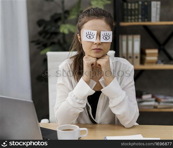 young businesswoman covering her eyes with drawn eyes paper