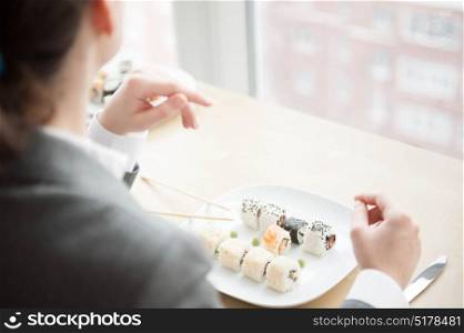 Young businesswoman eats sushi in formal dress