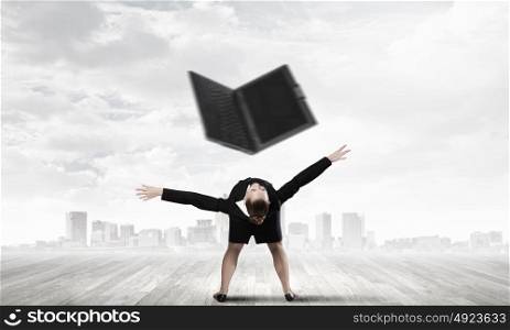 Young businesswoman evading back from flying laptop