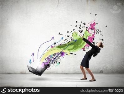 Young businesswoman evading colorful splashes flying from laptop. Impressive technology innovations
