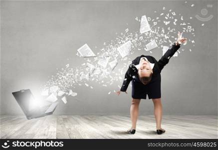 Young businesswoman evading papers flying from laptop. Super businesswoman