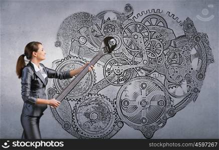 Young businesswoman fixing gears mechanism with wrench. Make it work