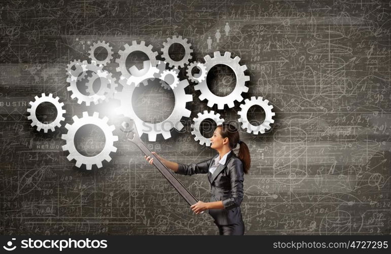 Young businesswoman fixing gears mechanism with wrench. Make it work