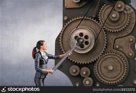 Young businesswoman fixing gears mechanism with wrench. Make it work