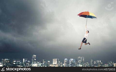 Young businesswoman flying high in sky on umbrella. Woman fly on umbrella