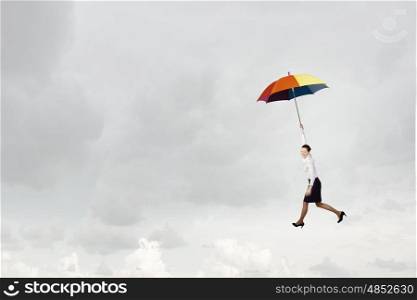 Young businesswoman flying high in sky on umbrella. Woman fly on umbrella