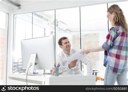 Young businesswoman giving documents to colleague at office