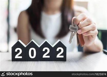 Young Businesswoman hands holding key and 2022 Happy New Year with house model on table office. New House, Financial, Property insurance, real estate, savings and New Year Resolution concepts