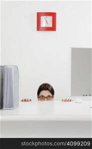 Young businesswoman hiding behind desk. Copy space