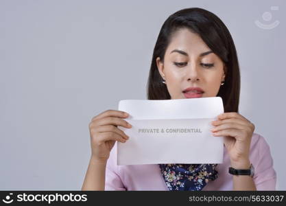 Young businesswoman holding confidential envelope against gray background