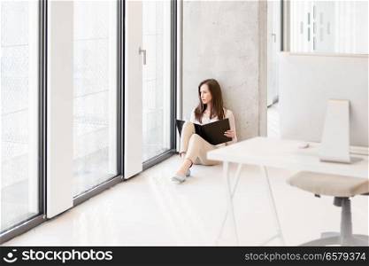 Young businesswoman holding file while sitting on floor in new office