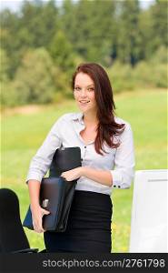 Young businesswoman in sunny nature behind table smiling carry briefcase