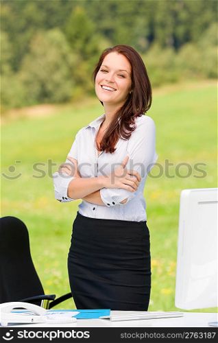 Young businesswoman in sunny nature behind table smiling crossed arms