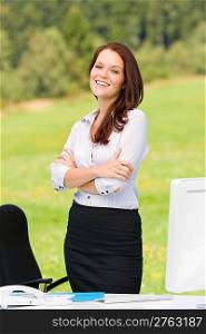 Young businesswoman in sunny nature behind table smiling crossed arms